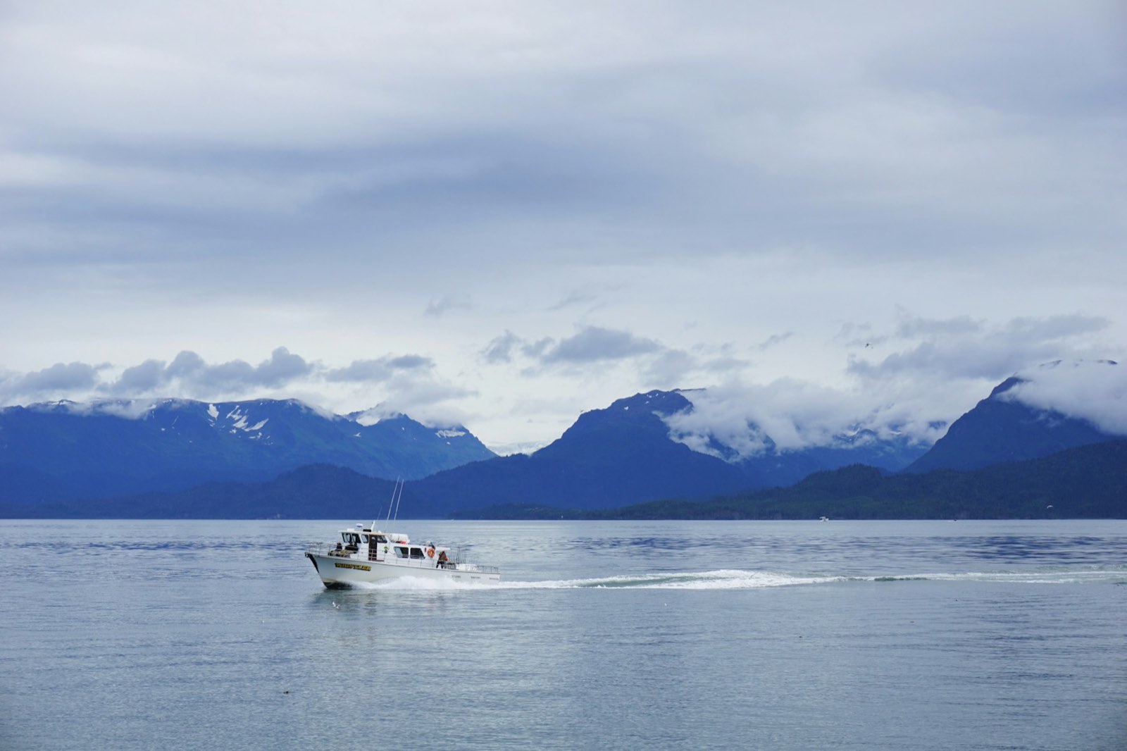 A small boat running below cloud-covered coastal mountains