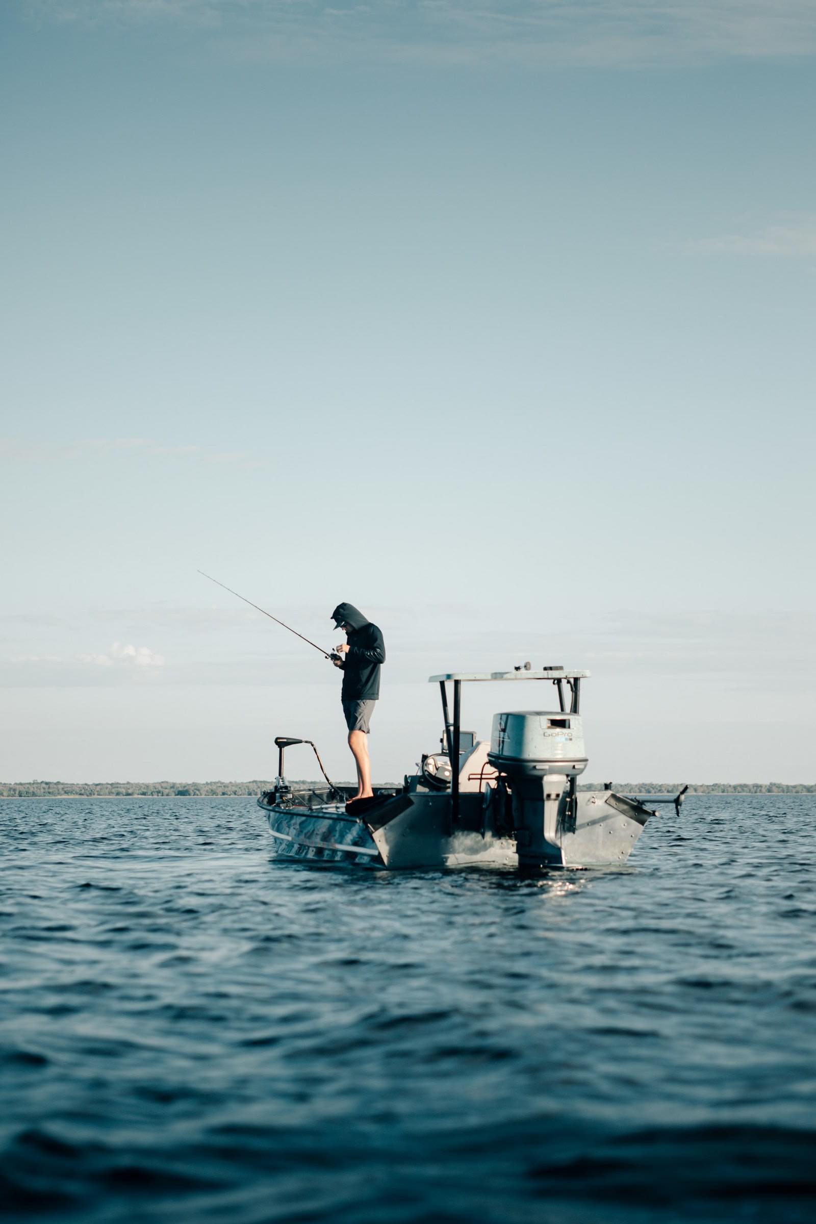 An angler working a rod from the deck of a small boat on calm coastal water